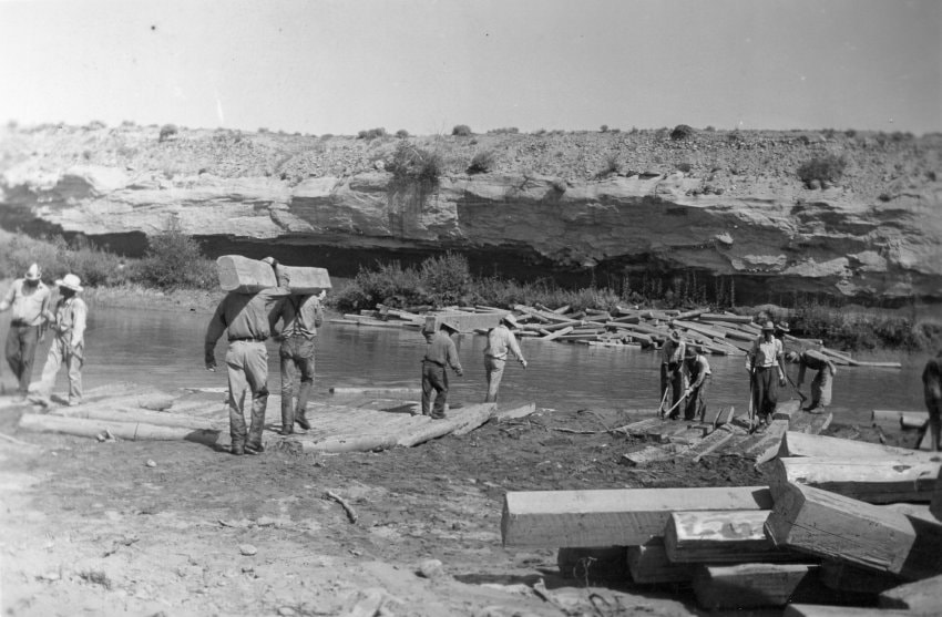 Historic workers carrying timber and working along the riverbank in Wind River Valley